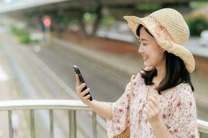 young asian woman traveler with weaving basket using mobile phone and standing on overpass with railway background. Journey trip lifestyle, world travel explorer or Asia summer tourism concept. photo