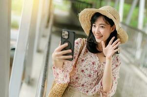 young asian woman traveler with weaving basket selfie with mobile phone and standing on overpass. Journey trip lifestyle, world travel explorer or Asia summer tourism concept. photo