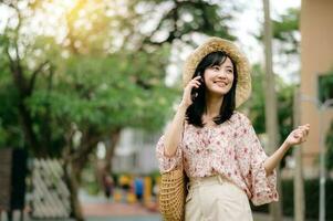 Portrait of asian young woman traveler with weaving hat and basket using mobile phone on green park nature background. Journey trip lifestyle, world travel explorer or Asia summer tourism concept. photo