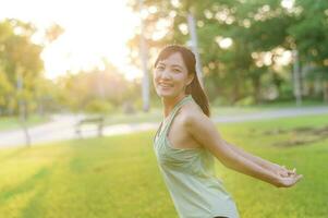 Female jogger. Fit young Asian woman with green sportswear breathing fresh air in park before running and enjoying a healthy outdoor. Fitness runner girl in public park. Wellness being concept photo
