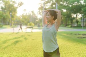 hembra persona que practica jogging. ajuste joven asiático mujer con verde ropa de deporte extensión músculo en parque antes de corriendo y disfrutando un sano exterior. aptitud corredor niña en público parque. bienestar siendo concepto foto