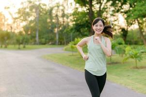 Fit Asian young woman jogging in park smiling happy running and enjoying a healthy outdoor lifestyle. Female jogger. Fitness runner girl in public park. healthy lifestyle and wellness being concept photo