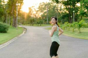 ajuste asiático joven mujer trotar en parque sonriente contento corriendo y disfrutando un sano al aire libre estilo de vida. hembra persona que practica jogging. aptitud corredor niña en público parque. sano estilo de vida y bienestar siendo concepto foto