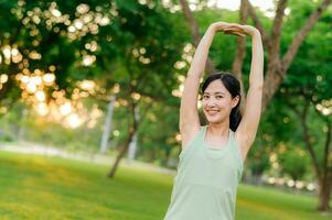 Female jogger. Fit young Asian woman with green sportswear stretching muscle in park before running and enjoying a healthy outdoor. Fitness runner girl in public park. Wellness being concept photo