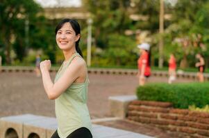 hembra persona que practica jogging. ajuste joven asiático mujer con verde ropa de deporte aeróbicos danza ejercicio en parque y disfrutando un sano exterior. aptitud corredor niña en público parque. bienestar siendo concepto foto