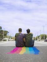 Boys couple sitting on the rainbow colored road. photo