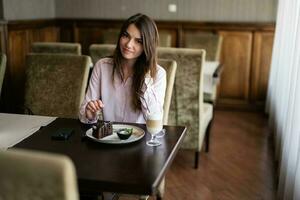 Young beautiful brunette woman sit in coffee shop cafe restaurant indoors and eat chocolate brownie dessert cake. photo