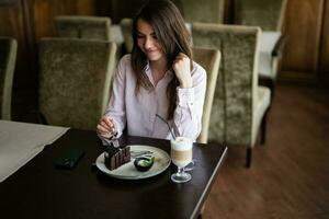 Young beautiful brunette woman sit in coffee shop cafe restaurant indoors and eat chocolate brownie dessert cake. photo