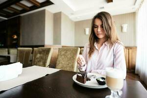 Young beautiful brunette woman sit in coffee shop cafe restaurant indoors and eat chocolate brownie dessert cake. photo