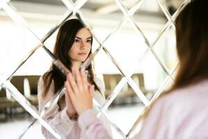 Young beautiful brunette woman in shirt touching mirror made of rhombuses. photo