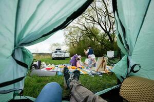 Father legs from tent. Happy young family, mother and children having fun and enjoying outdoor on picnic blanket painting at garden spring park, relaxation. photo