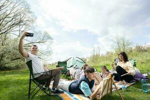 Dad runs a vlog. Happy young family having fun and enjoying outdoor on picnic blanket at garden spring park, relaxation. photo