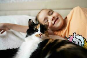 pequeño niña acostado en el cama con su gato y mirando a cámara foto