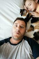 Top view of father and daughter sleeping together on the bed at home with cat and having fun. photo