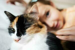 linda pequeño niña espectáculo lengua con su gato a hogar, de cerca foto