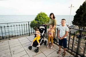 Portrait of happy mother with kids standing on promenade near sea. photo