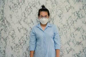 mujer pone en un cara máscara en pie con cruzado brazos proteger desde virus durante cuarentena aislado en blanco antecedentes,pandemia y social distanciamiento concepto foto