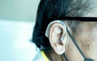 An old man wears a hearing aid, closeup photo