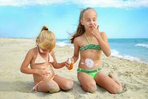 Sister applying protective sunscreen on young child. Girl draws sun cream on her stomach. photo