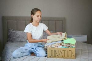 Girl holding donation box with with summer clothes. Selective focus on things in the box. photo