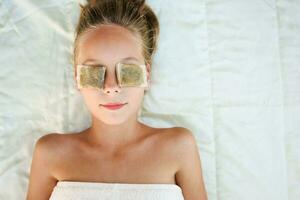 Beautiful girl with tea bags on eyes. Top view. photo