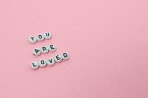 Top view of you are loved quotes made out of beads on pink background. motivation and success concept photo
