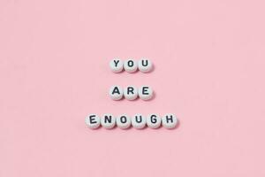 Top view of you are enough quotes made out of beads on pastel background. motivation and success concept photo