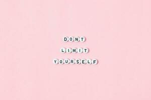 Top view of don't limit yourself quotes made out of beads on pink background. motivation and success concept photo