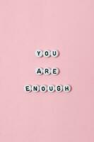 Top view of you are enough quotes made out of beads on pastel background. motivation and success concept photo