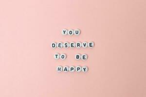 Top view of you deserve to be happy quotes made out of beads on pink background. motivation and success concept photo