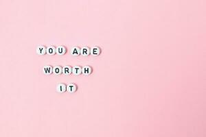 Top view of you are worth it quotes made out of beads on pastel background. motivation and success concept photo