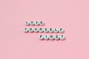 Top view of love yourself first quotes made out of beads on pink background. motivation and success concept photo