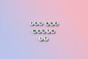 Top view of you are worth it quotes made out of beads on pastel background. motivation and success concept photo