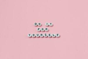 Top view of do it for yourself quotes made out of beads on pink background. motivation and success concept photo