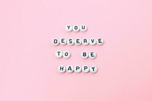 Top view of you deserve to be happy quotes made out of beads on pink background. motivation and success concept photo