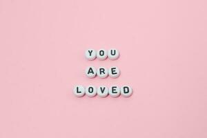 Top view of you are loved quotes made out of beads on pink background. motivation and success concept photo