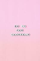 Top view of do it for yourself quotes made out of beads on pink background. motivation and success concept photo