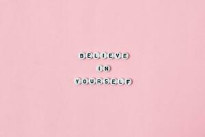 Top view of believe in yourself quotes made out of beads on pink background. motivation and success concept photo