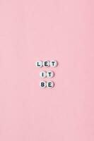 Top view of let it be quotes made out of beads on pink background. motivation and success concept photo