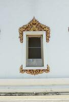 A golden and red color frame ancient native Thai style of white painted wood windows on white painted cement wall church in temple, Bangkok, Thailand. photo