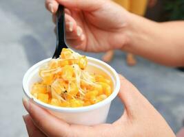 Corn and melt cheese stretches in white cup with hand hold black plastic spoon. photo