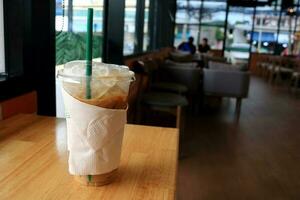 Ice coffee in plastic glass surround by paper napkins on brown wood table in cafe. photo