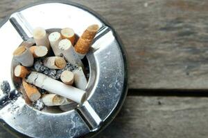 Top view of round shape stainless ashtray on wood plank and tobacco with ash in ashtray. photo