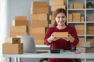 Starting small business entrepreneur of independent Asian woman smiling using computer laptop with cheerful success of online marketing package box items and SME delivery concept photo