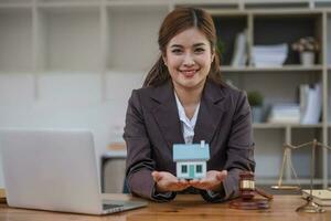 Beautiful Asian businesswoman lawyer sitting at the office holding a pen taking note working on a loan a sample home mallet a laptop at the table. photo