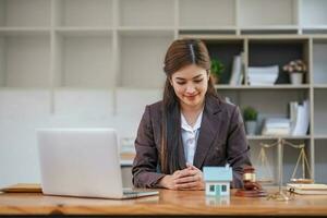 Beautiful Asian businesswoman lawyer sitting at the office holding a pen taking note working on a loan a sample home mallet a laptop at the table. photo