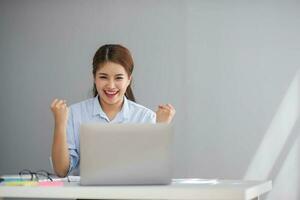 asiático mujer de negocios espectáculo alegre expresión de éxito a trabajo sonriente felizmente con un ordenador portátil computadora en un moderno oficina. foto