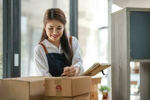 Startup small business entrepreneur SME, asian woman packing cloth in box. Portrait young Asian small business owner home office, online sell marketing delivery, SME e-commerce telemarketing concept photo