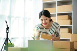 emprendedor de pequeñas empresas pyme autónomo, retrato de mujer joven que trabaja en la oficina en casa, caja, teléfono inteligente, computadora portátil, en línea, marketing, empaque, entrega, b2b, pyme, concepto de comercio electrónico. foto