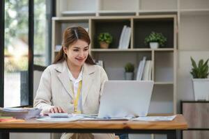 Asian Businesswoman Using laptop computer and working at office with calculator document on desk, doing planning analyzing the financial report, business plan investment, finance analysis concept. photo